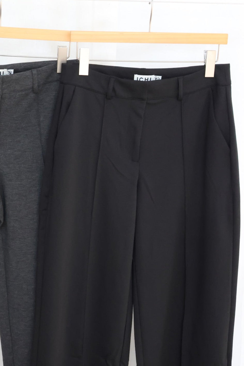 Two pairs of black pants hanging on a rack against a white background