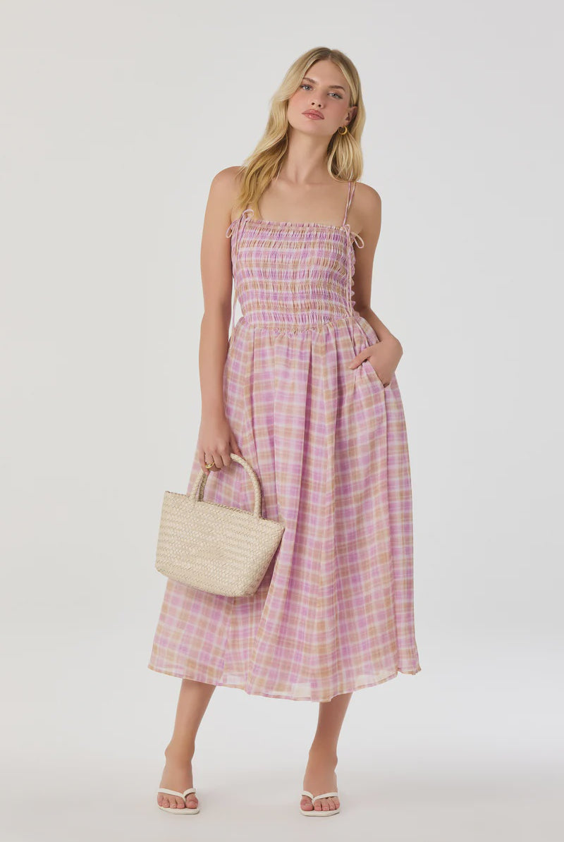 Woman wearing a pink plaid dress holding a beige handbag on a white background