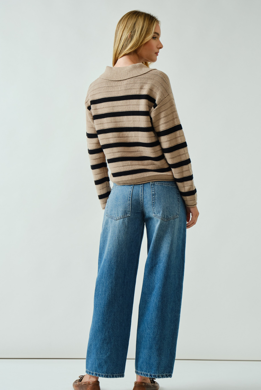 Woman wearing a striped sweater and blue jeans against a white background