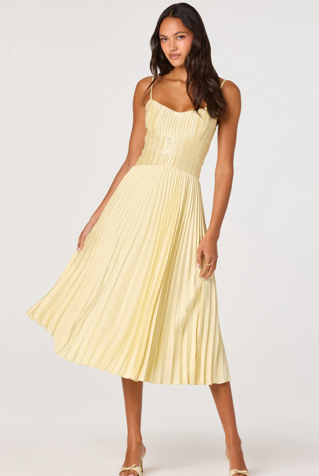 Woman wearing a light yellow pleated dress on a white background