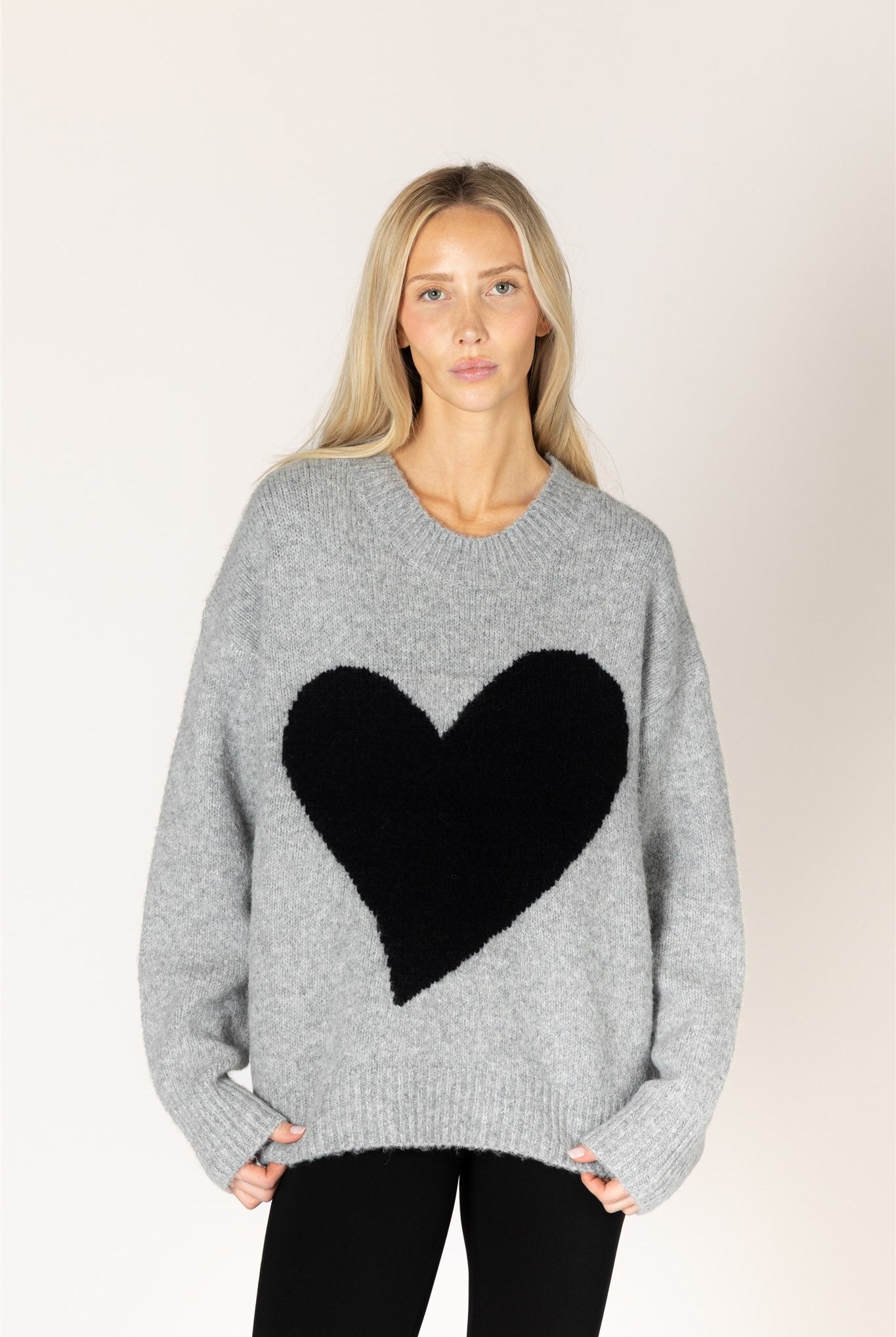 Dark grey oversized crewneck sweater featuring a bold black heart graphic on the front, with ribbed cuffs and hem.