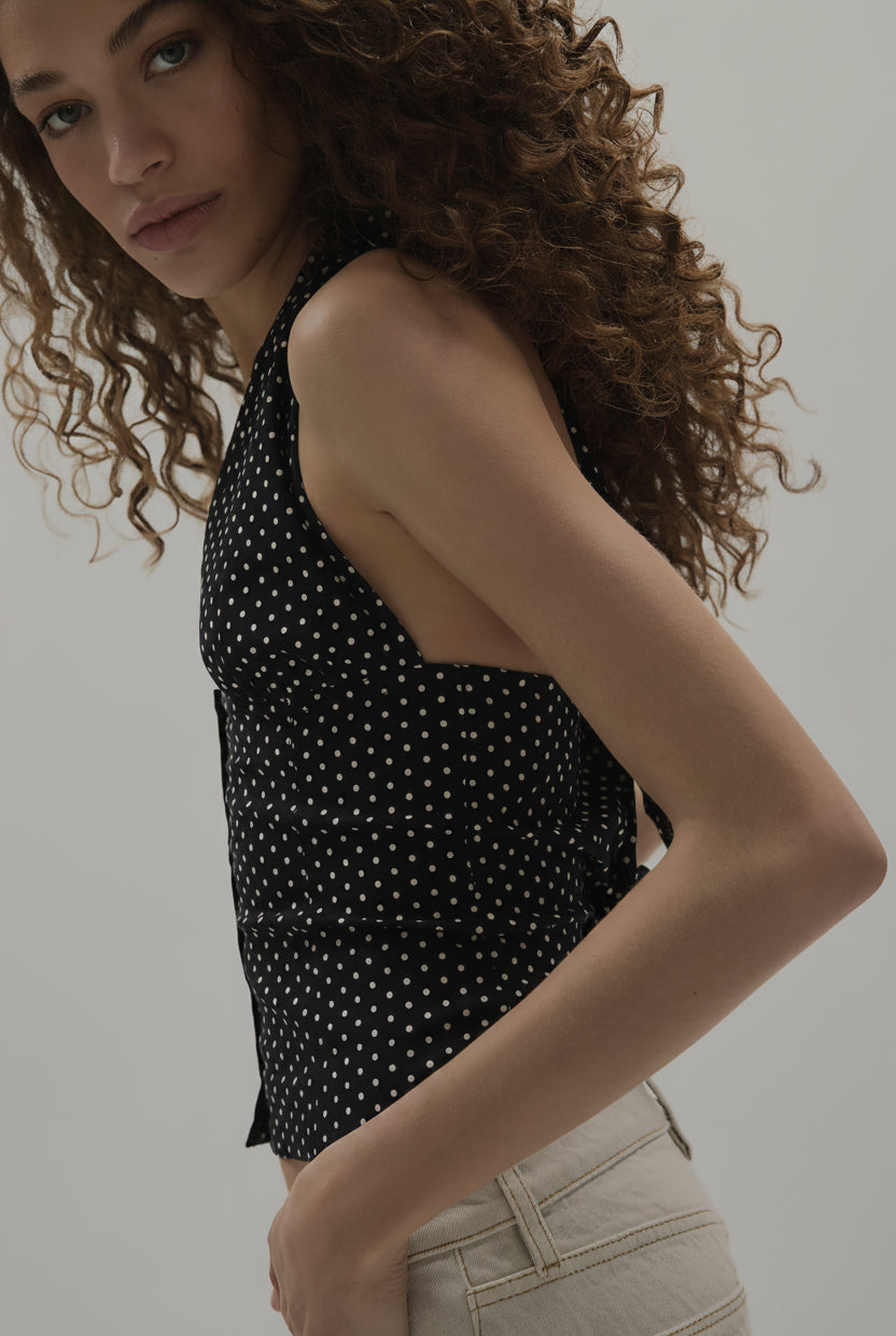 Woman wearing a black sleeveless top with white polka dots against a plain background