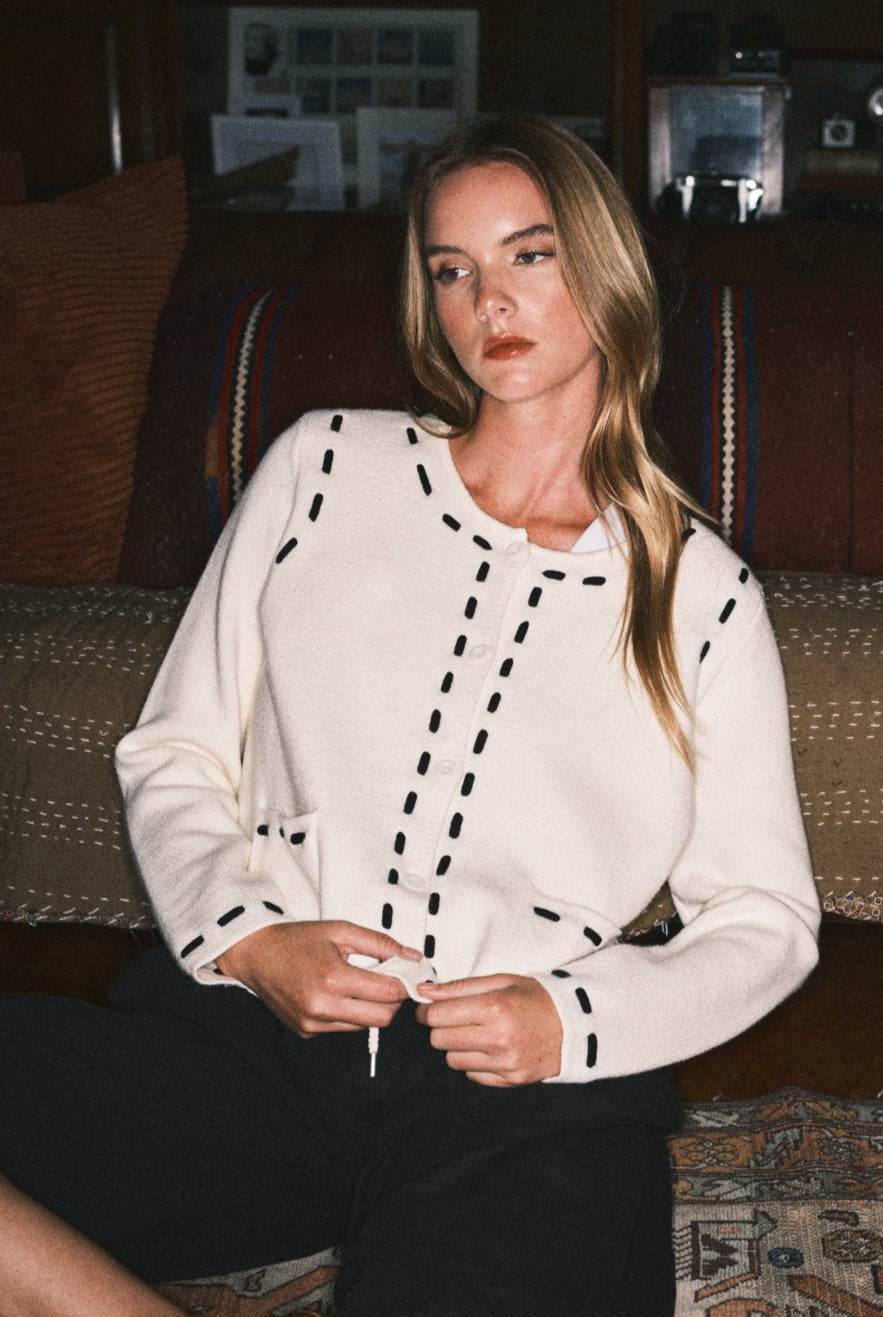 Woman wearing a white blouse with black patterns sitting on a patterned rug.