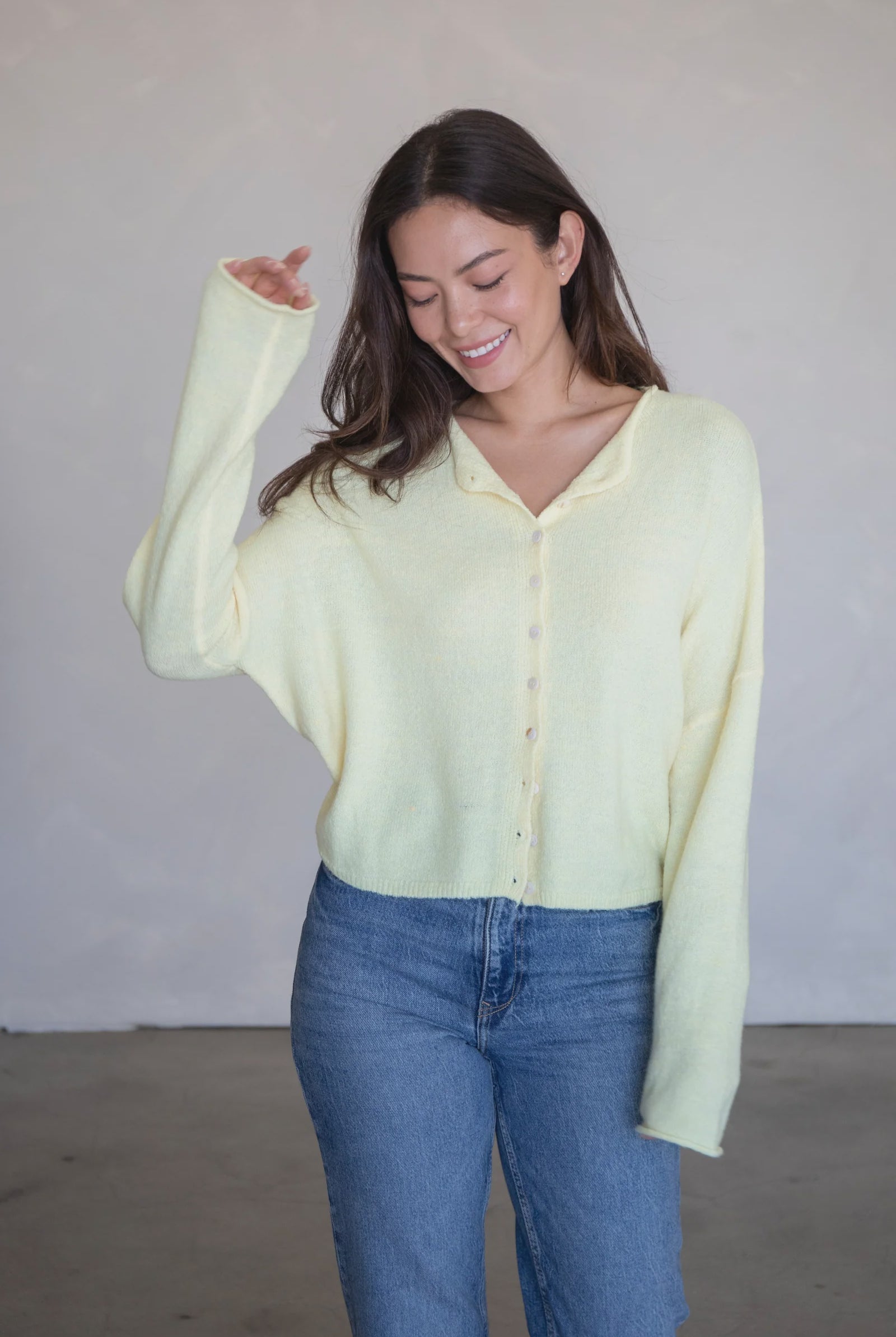 Woman wearing a light yellow shirt and blue jeans against a plain background