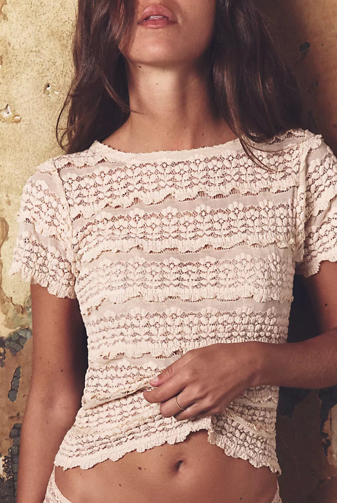Woman wearing a lace top against a textured wall.