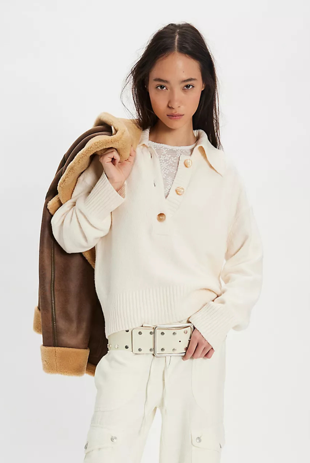 Woman wearing a cream-colored coat with a brown leather jacket over her shoulder on a white background