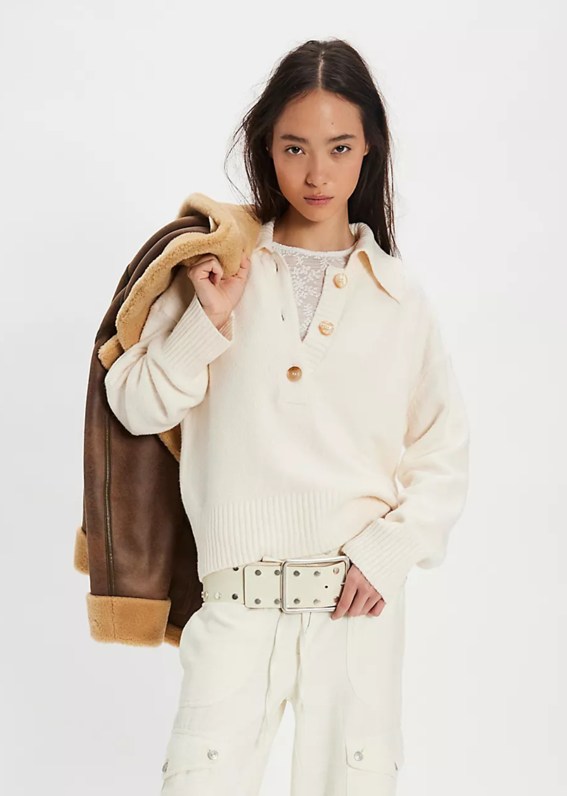 Woman wearing a cream-colored coat with a brown leather jacket over her shoulder on a white background