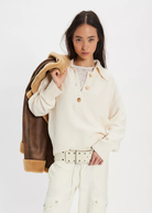 Woman wearing a cream-colored coat with a brown leather jacket over her shoulder on a white background