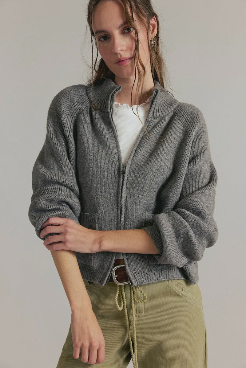 Women's ribbed knit zip-front sweater in cool grey with a high turtleneck collar, raglan sleeves, and front patch pockets.
