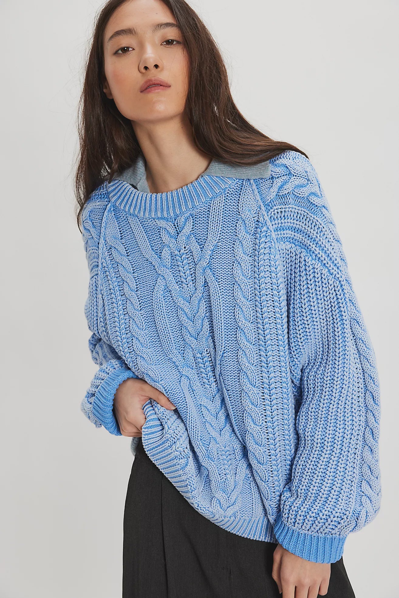 Woman wearing a blue cable knit sweater against a white background