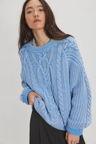 Woman wearing a blue cable knit sweater against a white background