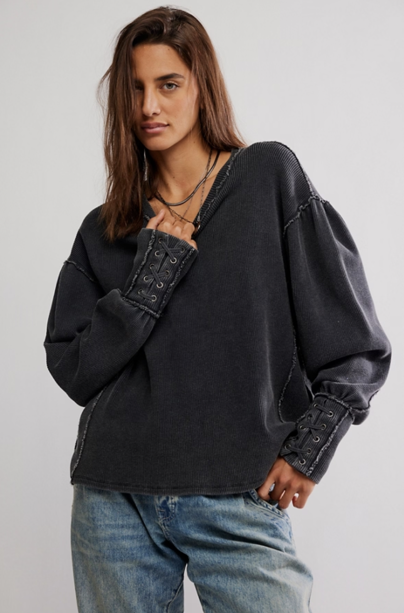 Woman wearing a black oversized sweater with button details on a plain background