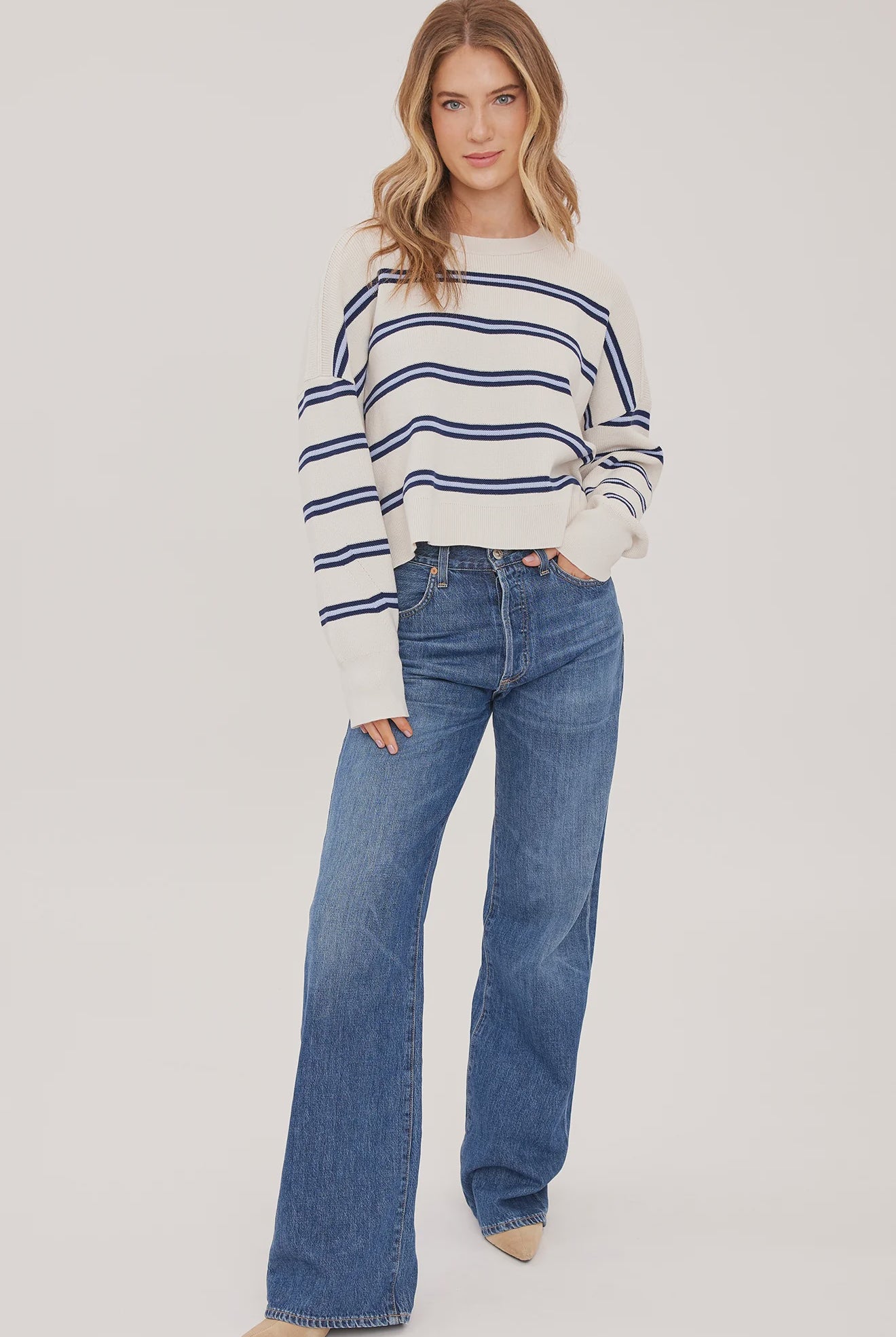 Woman wearing the Gentle Fawn Echo Sweater in Cream Stripe, featuring a super soft knit, oversized fit, half-cardigan stitch, exposed seam detailing, side slits, and classic cream striped pattern.