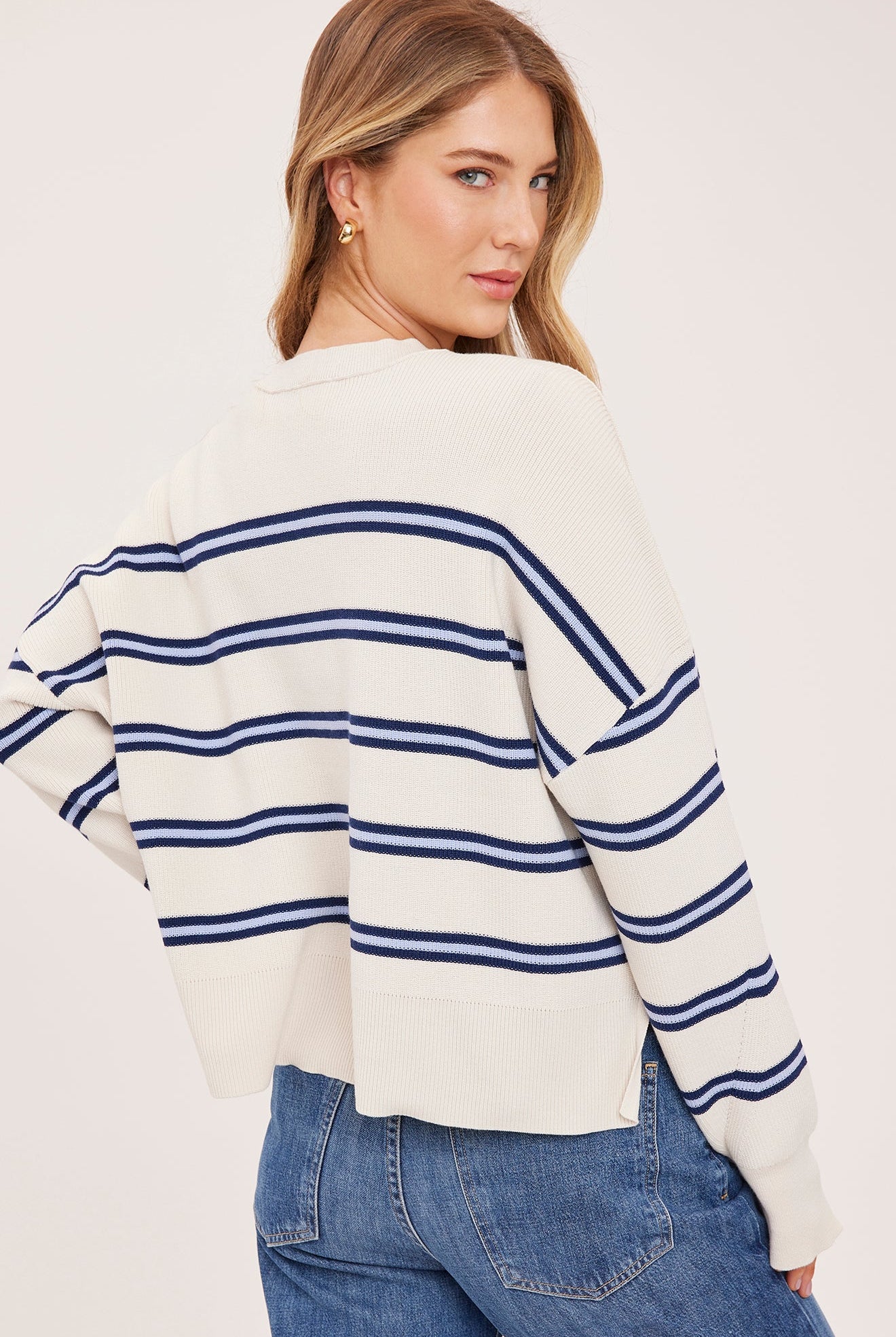 Woman wearing the Gentle Fawn Echo Sweater in Cream Stripe, featuring a super soft knit, oversized fit, half-cardigan stitch, exposed seam detailing, side slits, and classic cream striped pattern.