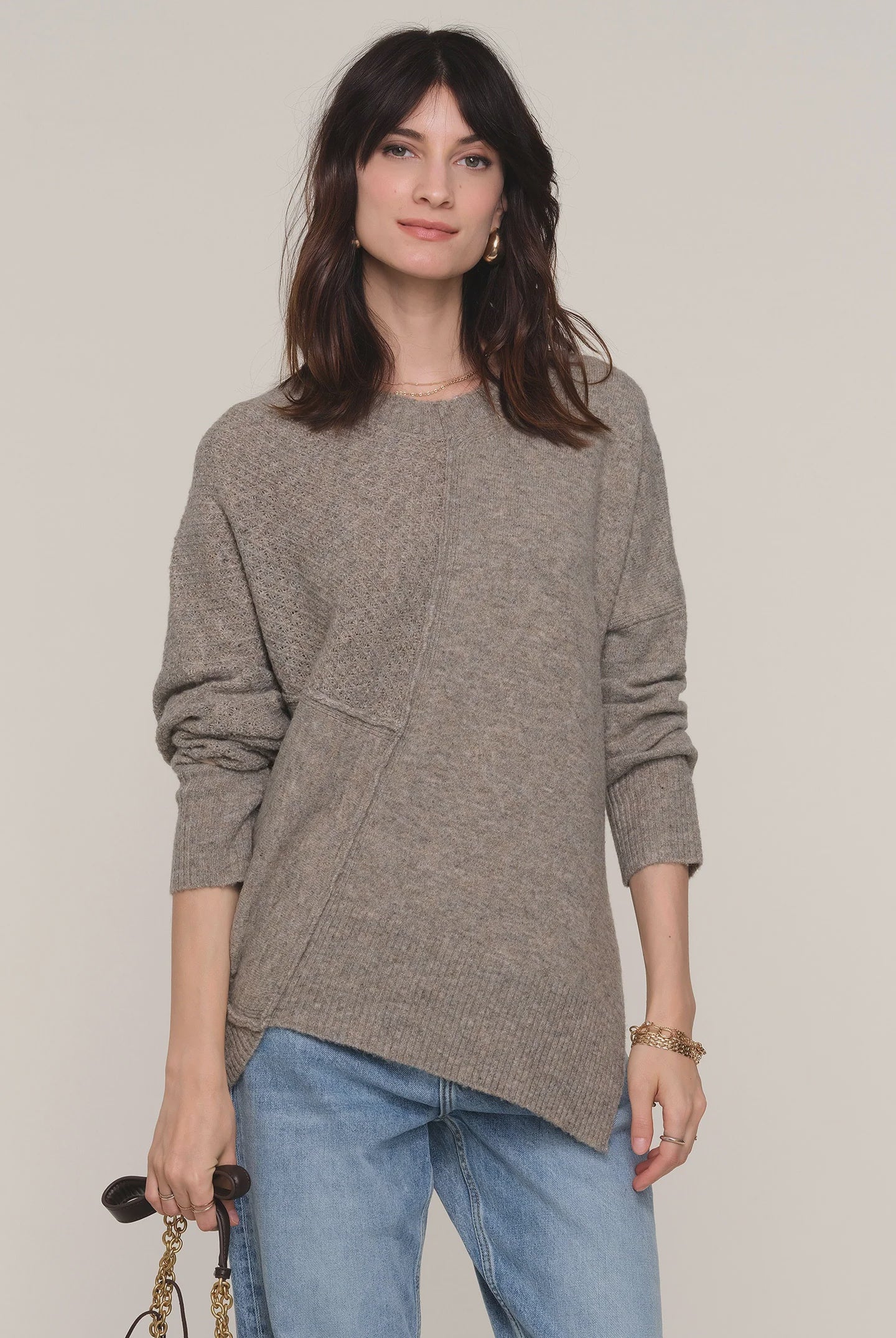 Woman wearing a gray sweater and blue jeans against a plain background