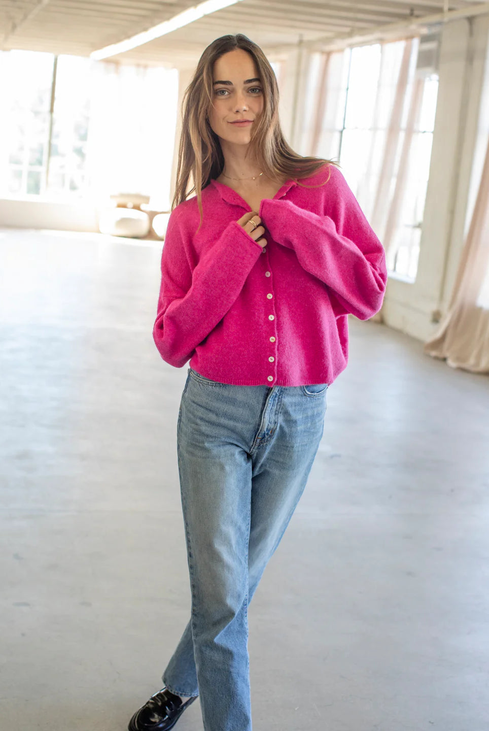 Woman wearing a bright pink sweater and blue jeans indoors.
