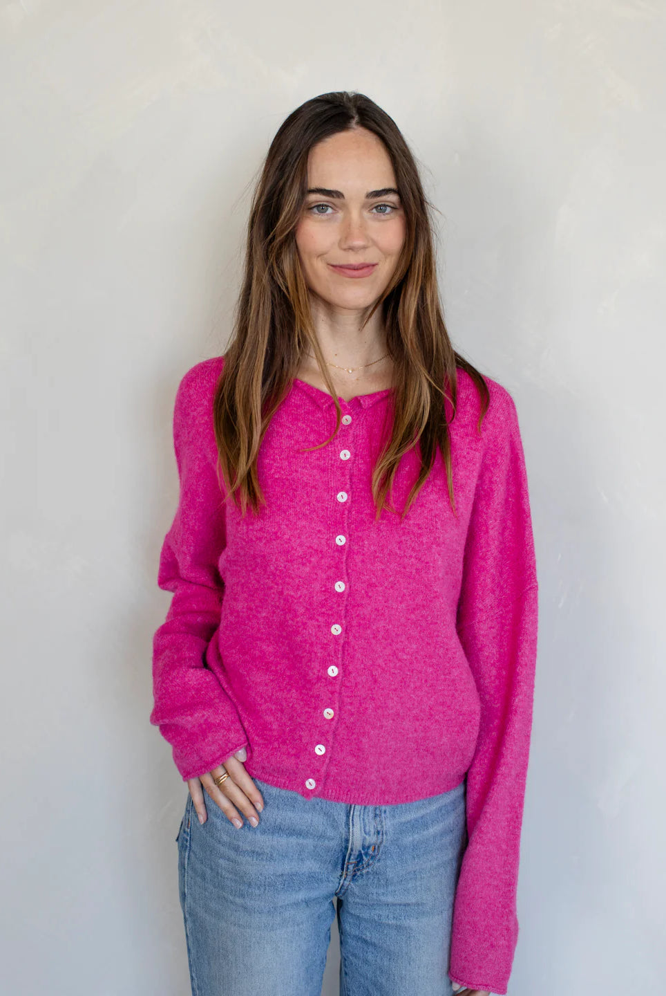 Woman wearing a bright pink cardigan against a plain background