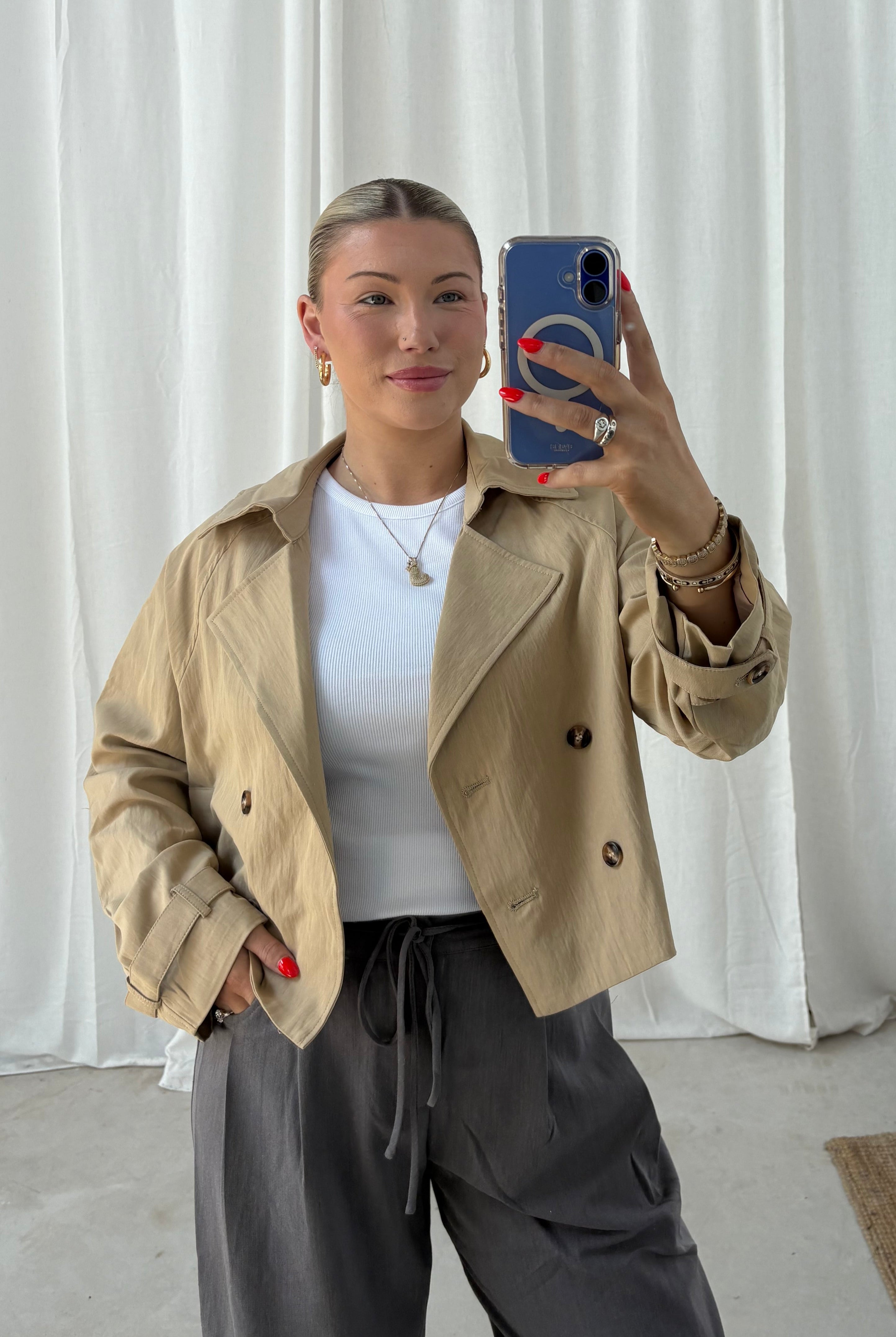 Person wearing a beige trench coat in front of a white curtain