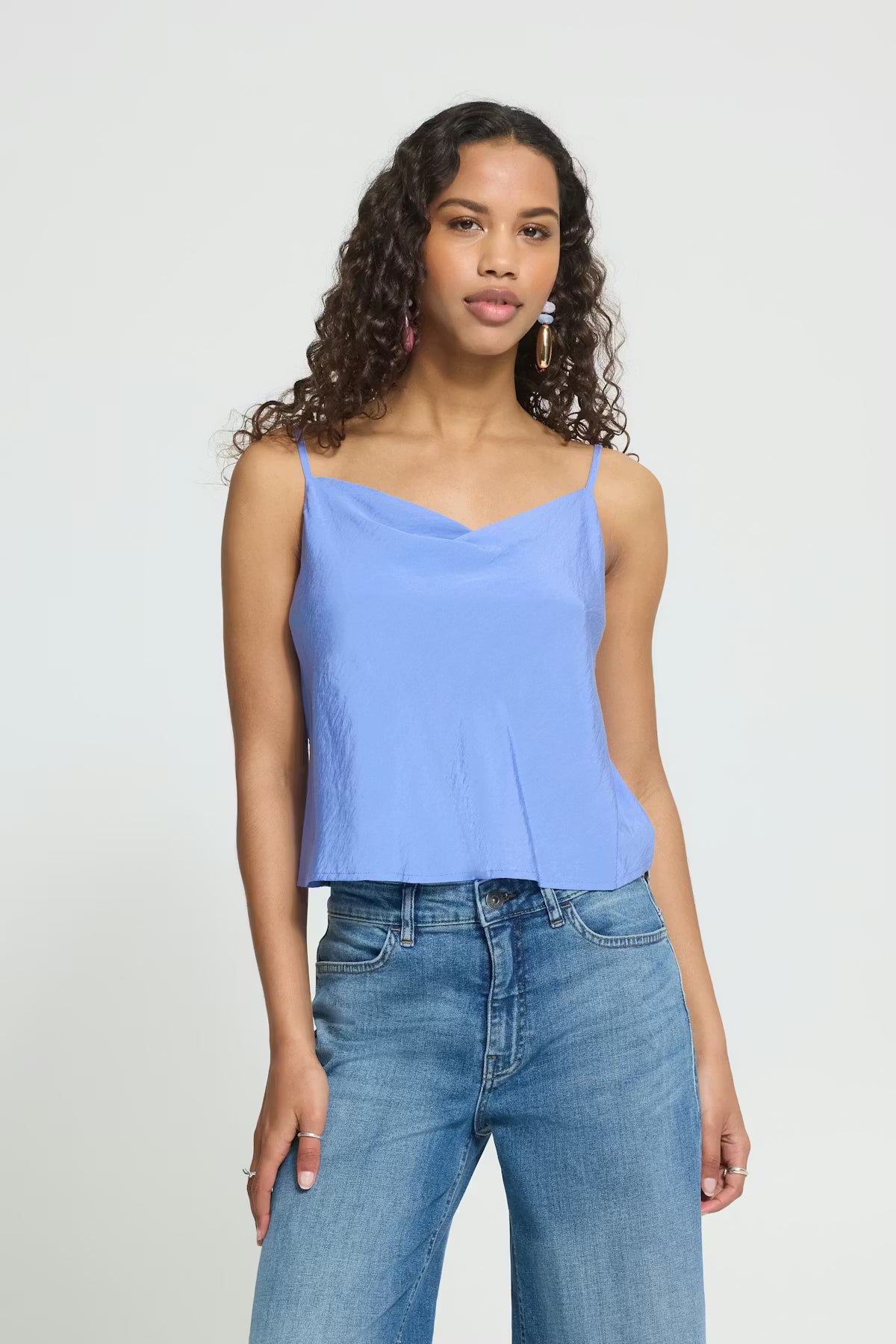 Woman wearing a light blue sleeveless top and blue jeans on a plain background