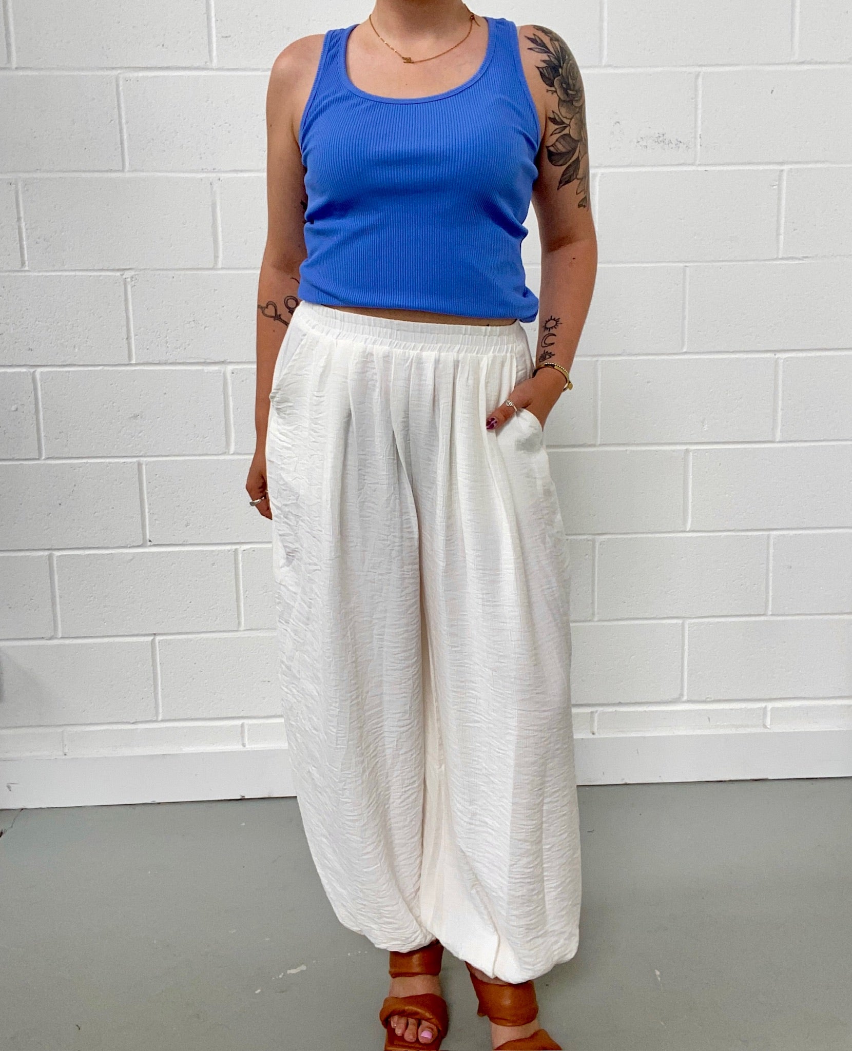 Person wearing a blue tank top and white balloon pants