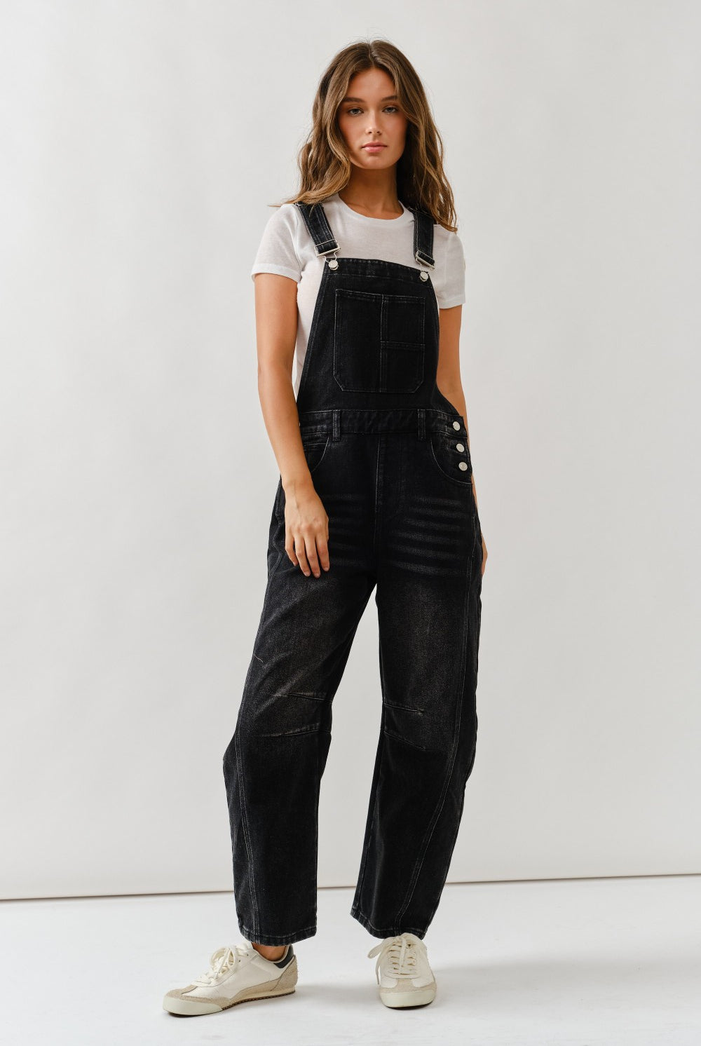 Woman wearing black overalls and a white t-shirt against a plain background
