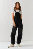 Woman wearing black overalls and a white t-shirt against a plain background