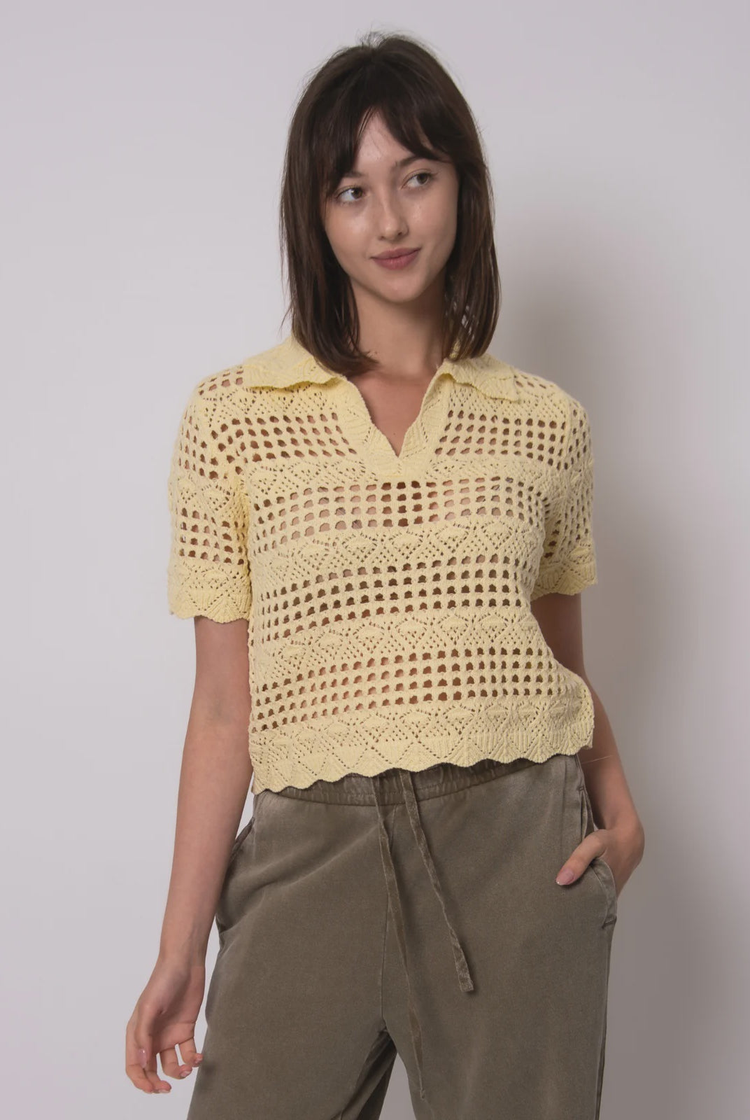 Woman wearing a yellow crochet top against a plain background