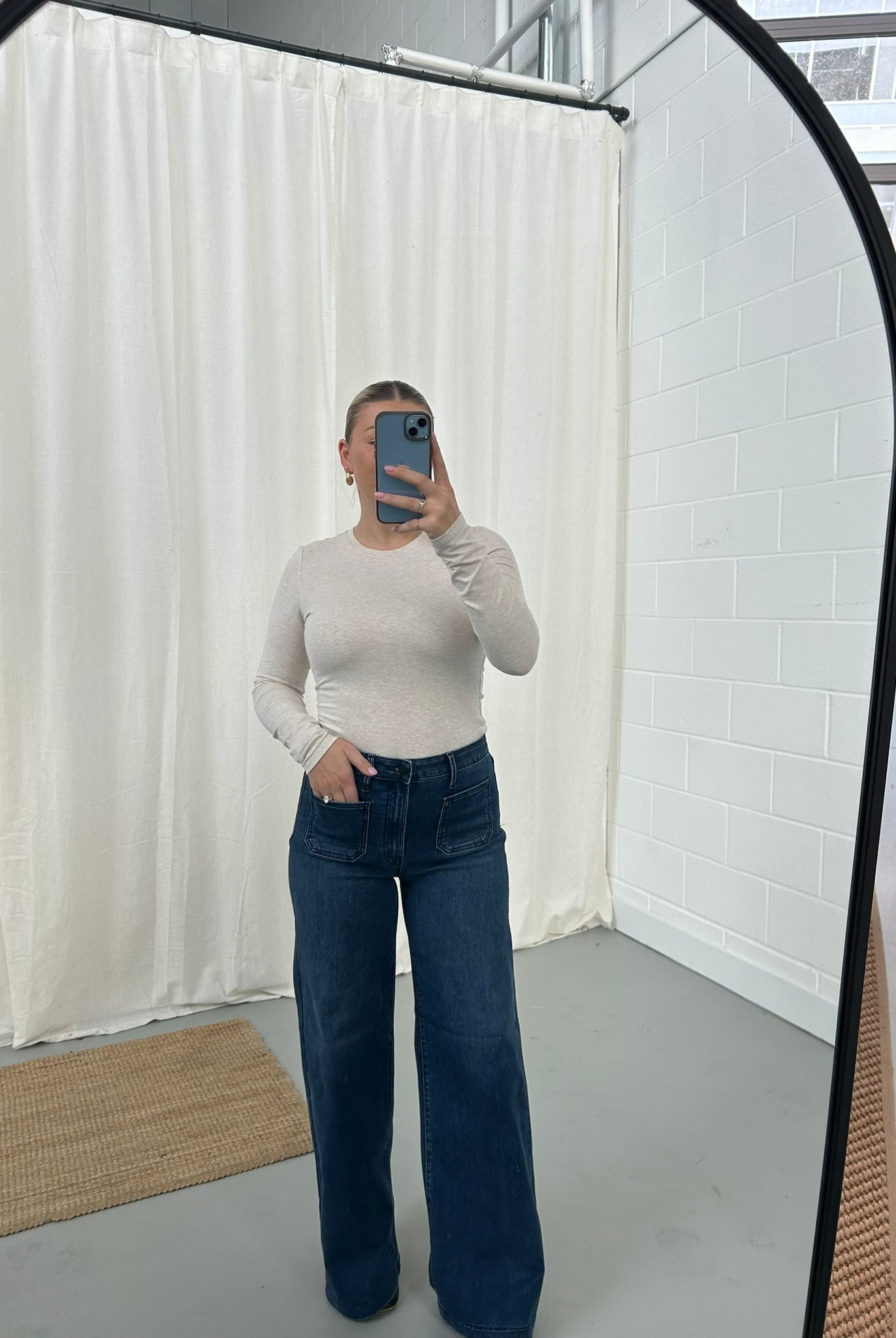 Person wearing a white long-sleeve top and blue jeans taking a mirror selfie.