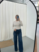 Person wearing a white long-sleeve top and blue jeans taking a mirror selfie.