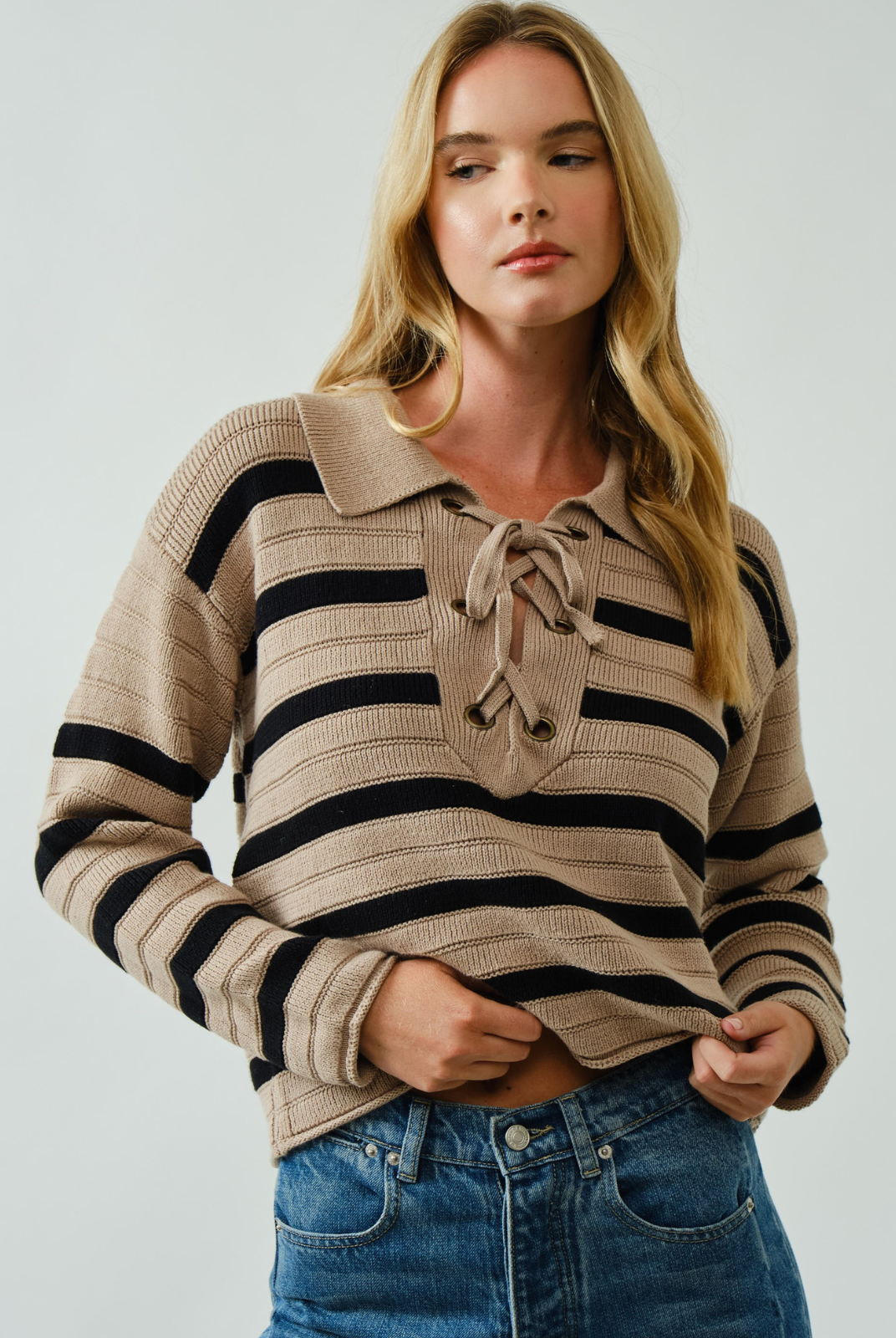 Woman wearing a striped sweater with a collar and tie detail on a plain background