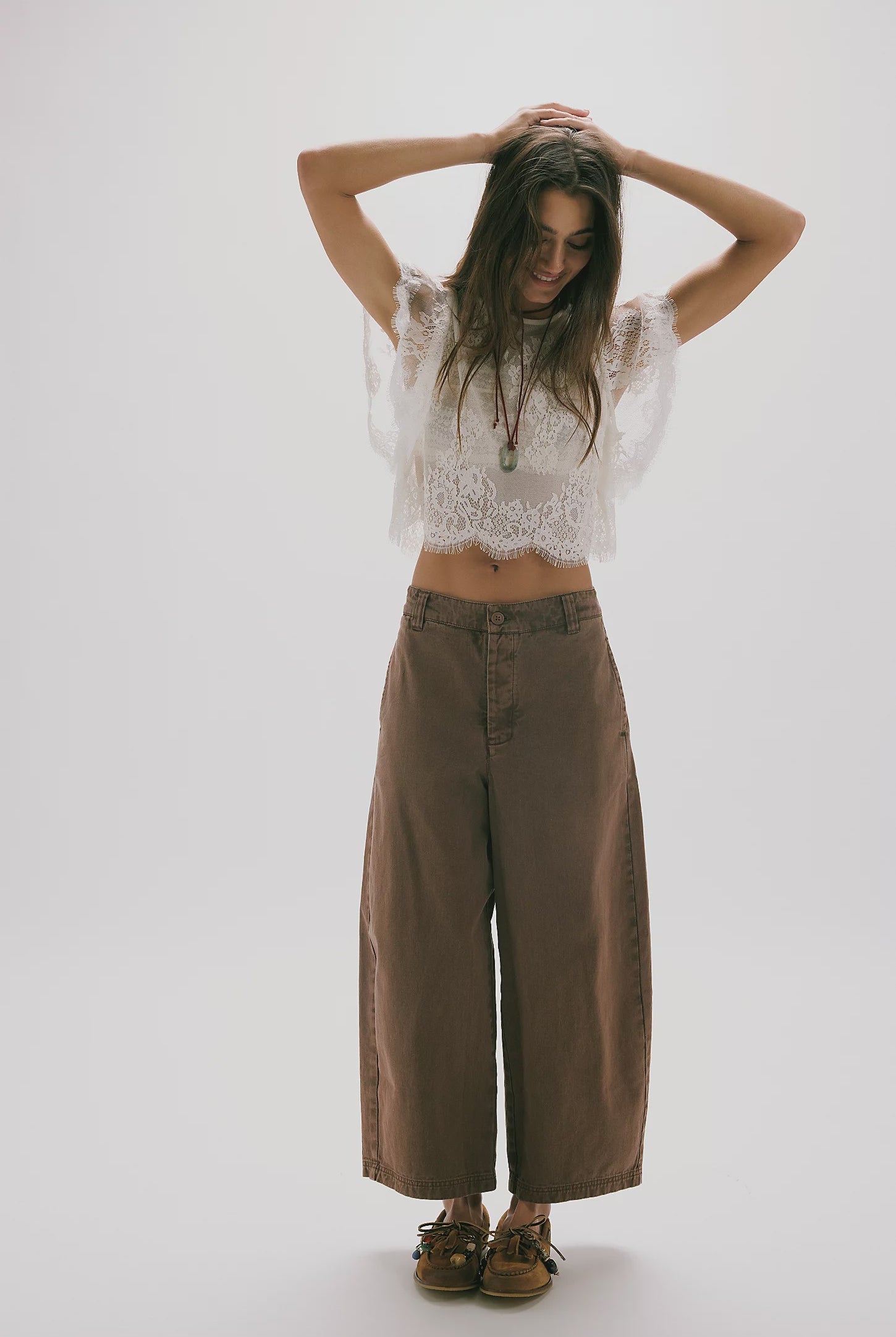 Woman wearing a white lace top and brown wide-leg pants on a white background