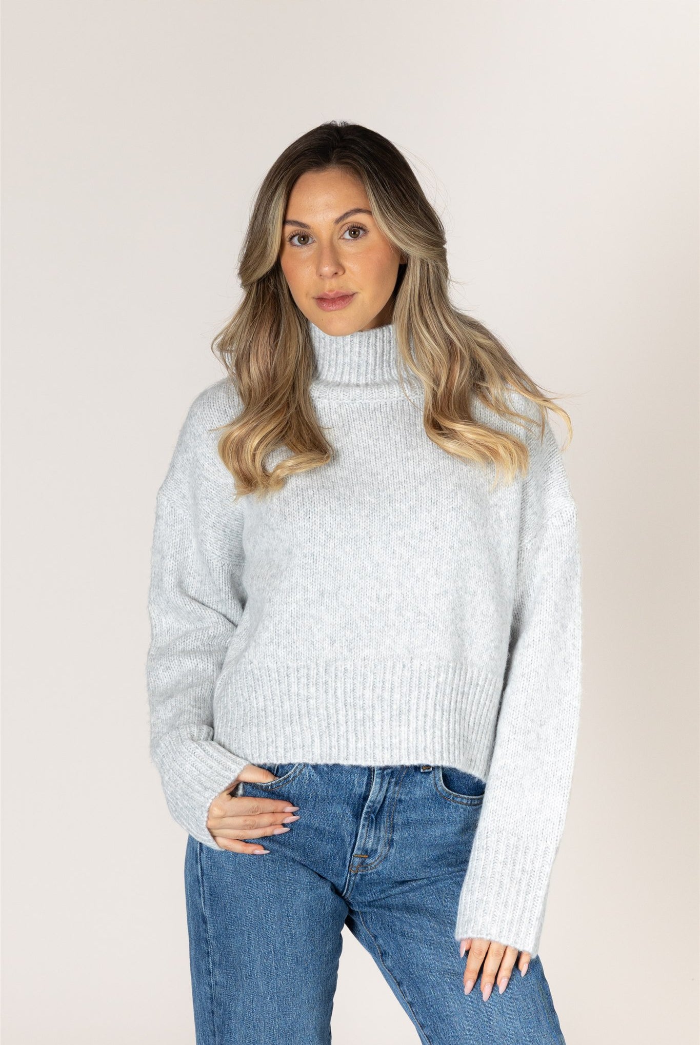 Light ash grey knit sweater featuring a mock neckline, relaxed fit, dropped shoulders, long sleeves, and ribbed cuffs and hem.