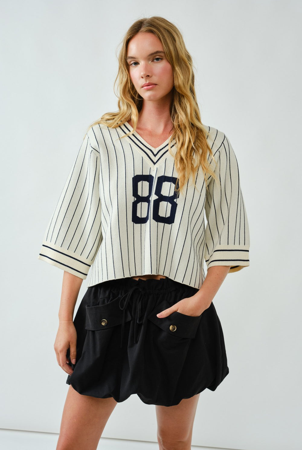 Woman wearing a striped baseball jersey with number 88 and black shorts against a white background
