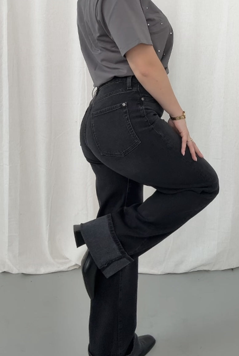 Person wearing black pants and a gray shirt against a white curtain background