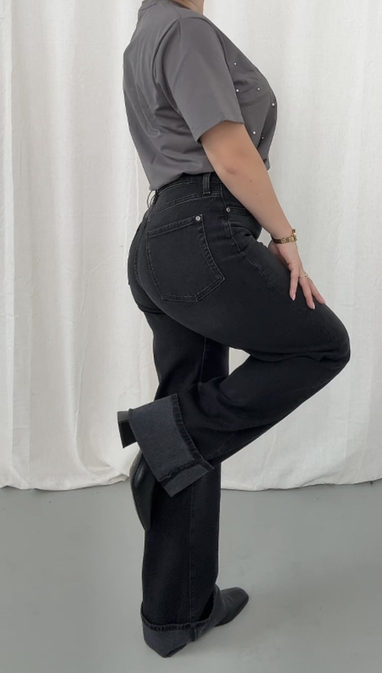 Person wearing black pants and a gray shirt against a white curtain background