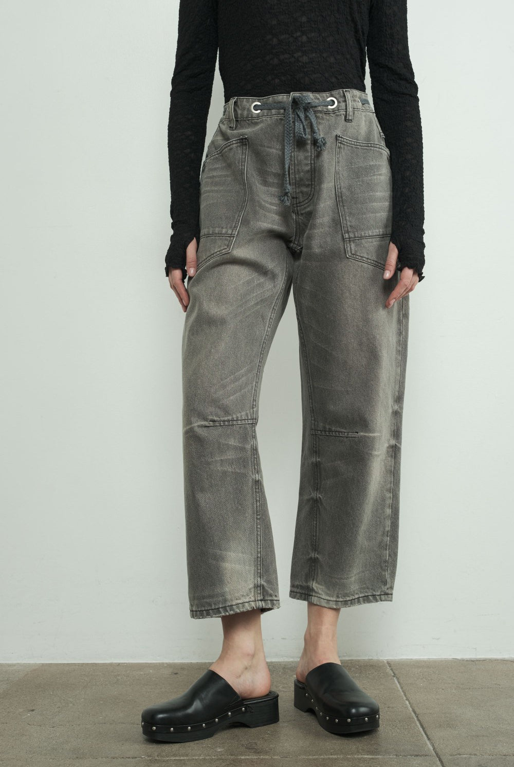 Person wearing dark gray jeans and black clogs on a plain background