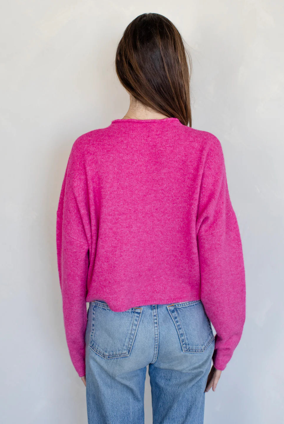 Person wearing a bright pink sweater and blue jeans against a plain background