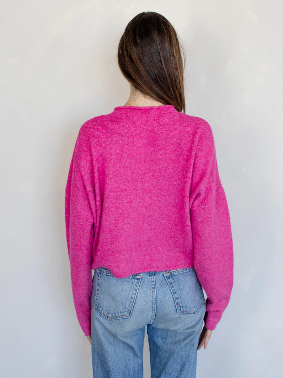 Person wearing a bright pink sweater and blue jeans against a plain background