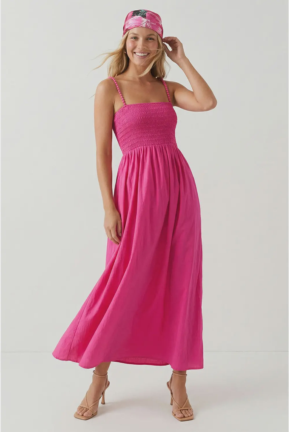 Hot pink maxi dress featuring a fitted smocked bodice, square neckline, adjustable pom pom shoulder straps, a flowing full-length skirt, and side pockets