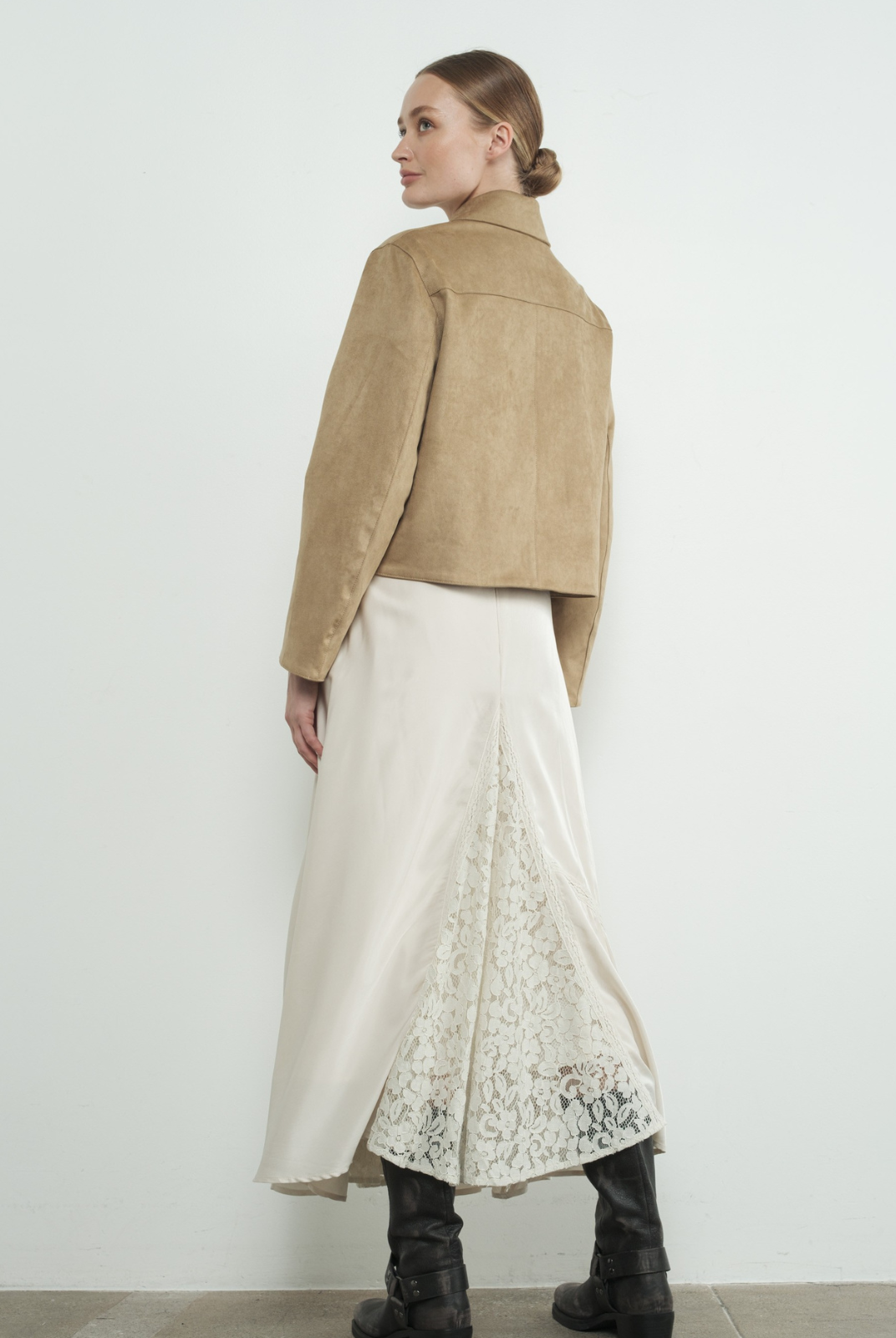 Woman wearing a beige jacket and white skirt with lace details against a white background