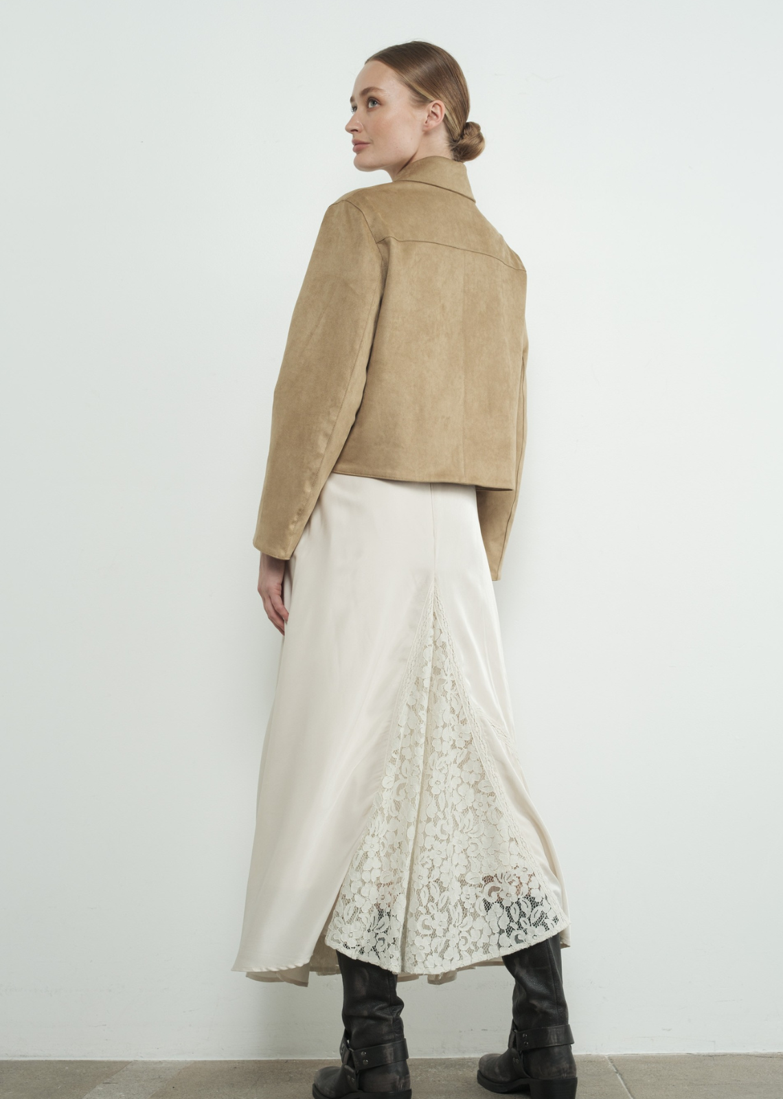 Woman wearing a beige jacket and white skirt with lace details against a white background