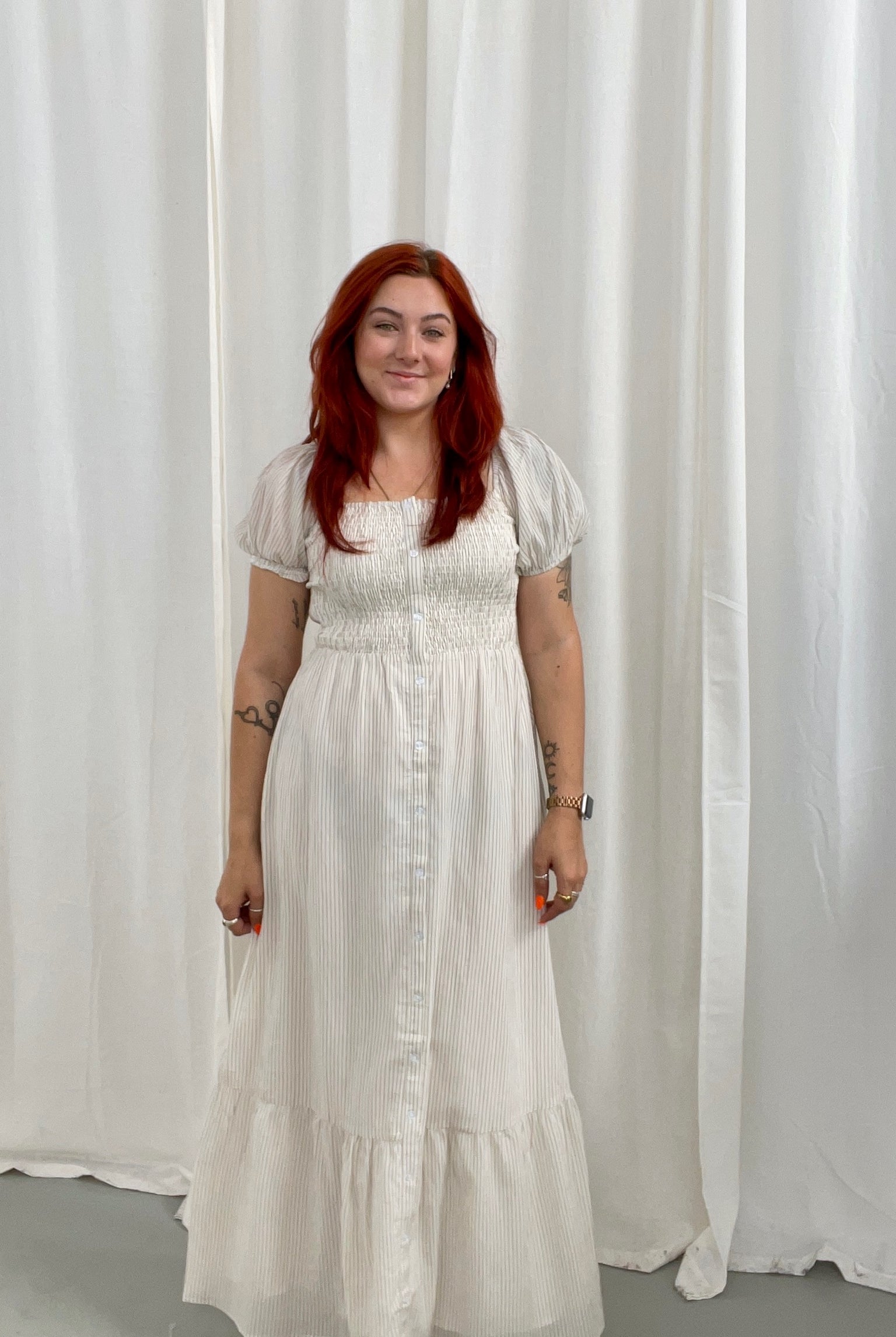 Woman wearing a white dress with light taupe stripes, soft puff sleeves and a button down detail