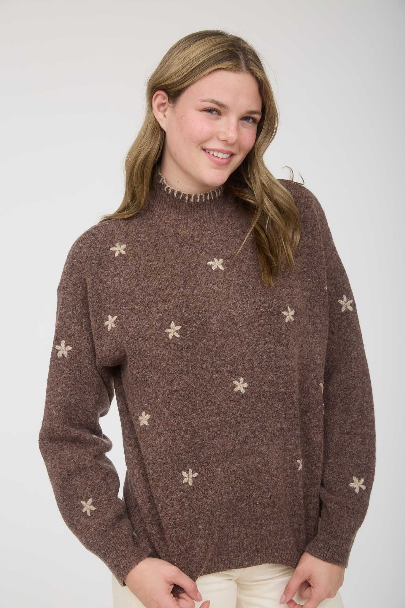 Woman wearing a brown sweater with star flower patterns on a white background