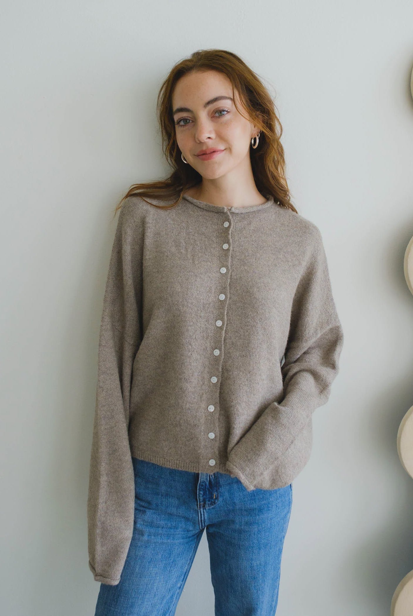 Woman wearing a beige cardigan and blue jeans against a light background