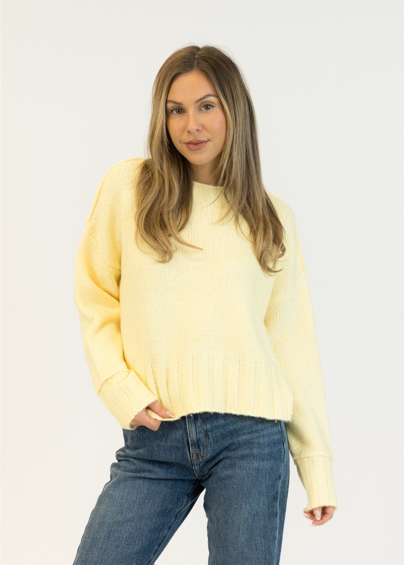 Woman wearing a light yellow sweater and blue jeans on a white background