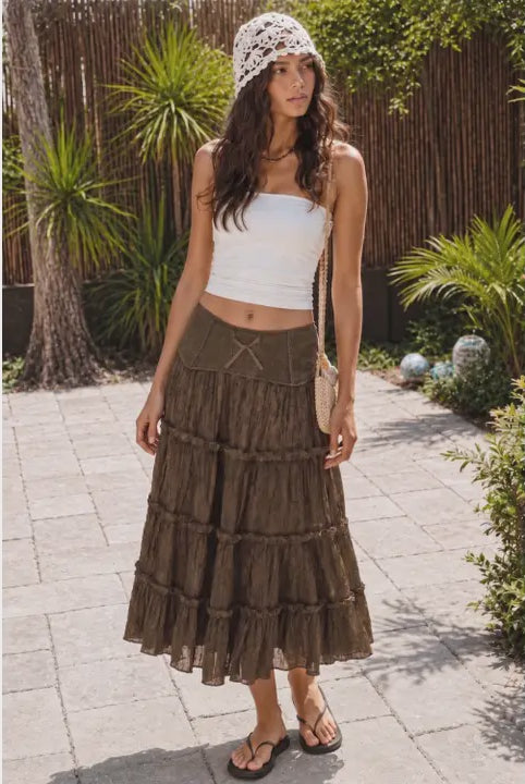 Model wearing The Savannah Lace Maxi Skirt, a brown crinkle maxi skirt featuring tiered ruffle panels, delicate lace trim, and a fitted waistband