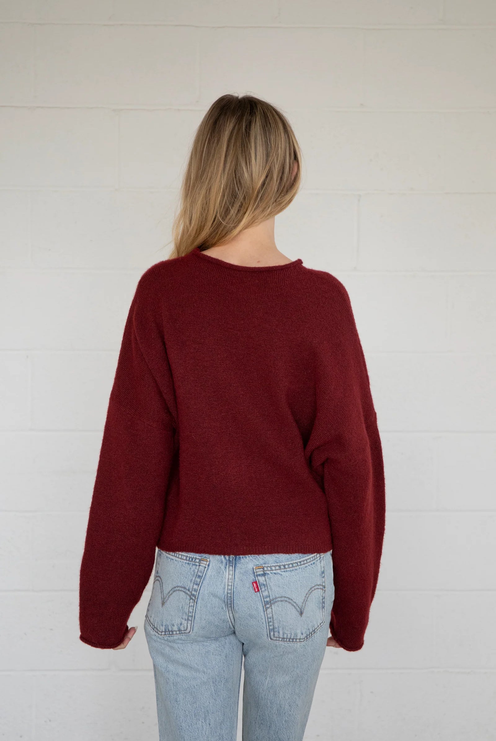 Person wearing a burgundy sweater and light blue jeans against a white wall