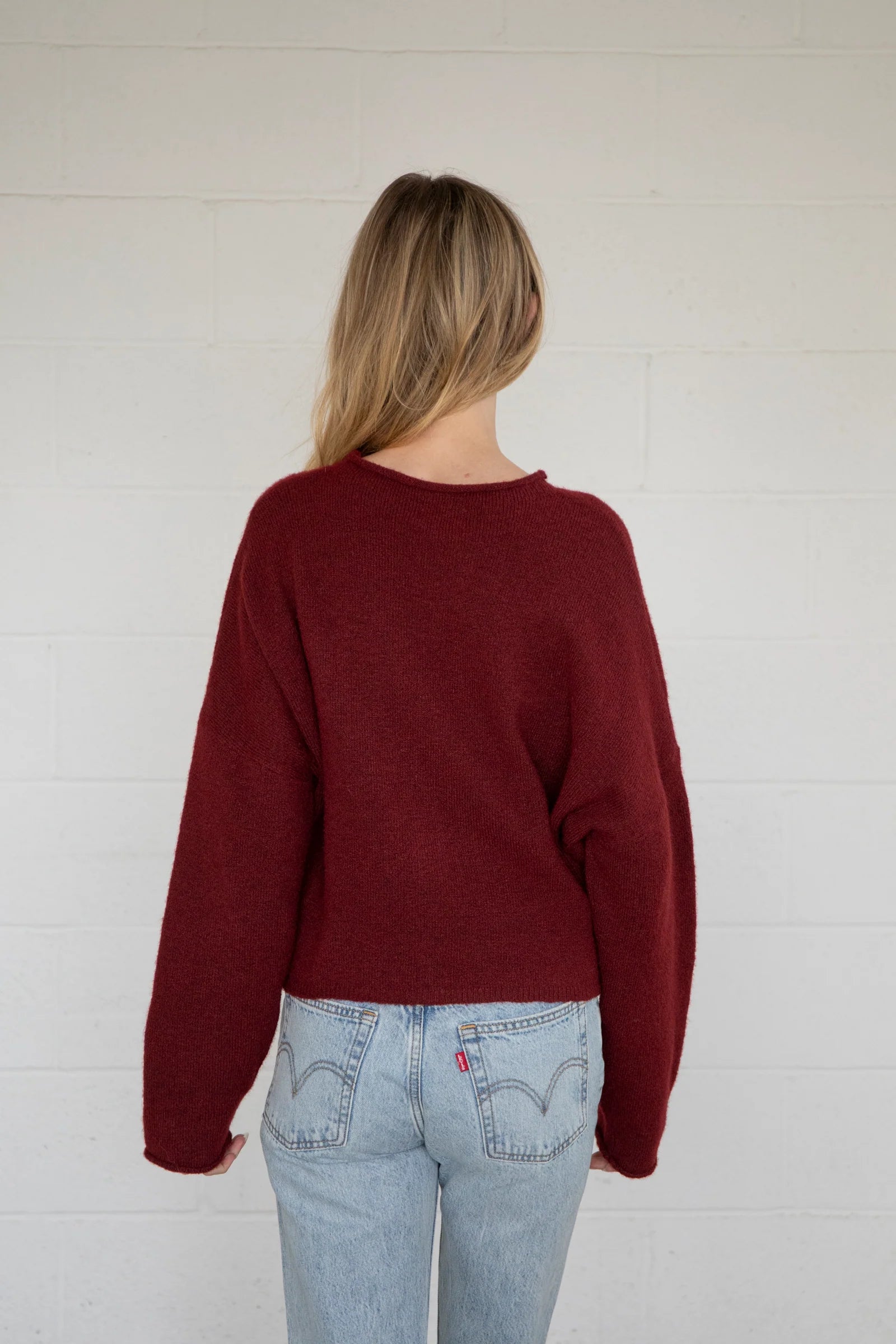 Person wearing a burgundy sweater and light blue jeans against a white wall
