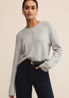 Woman wearing a gray sweater and black pants against a beige background