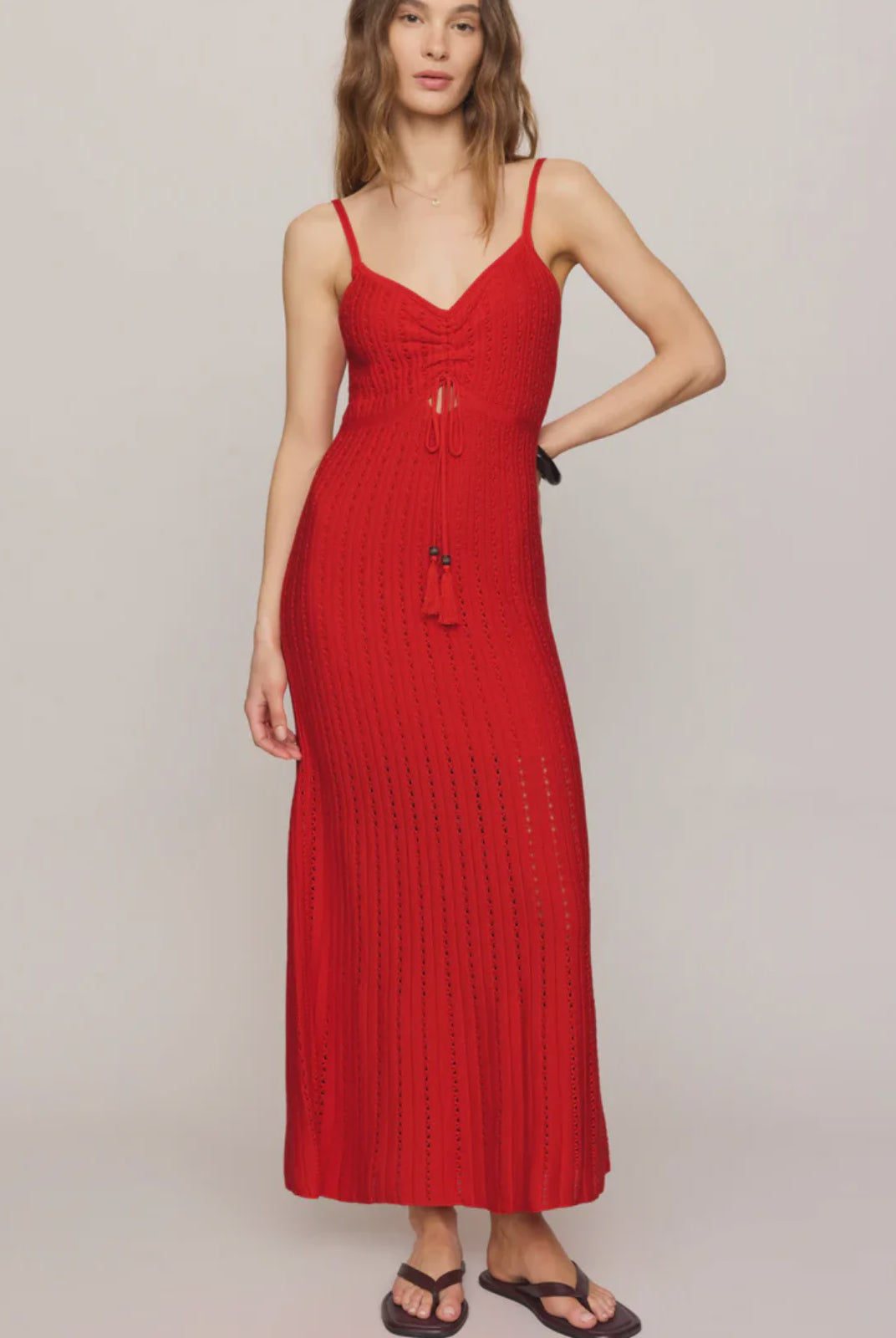 Woman wearing a red crochet dress with tassles against a plain background